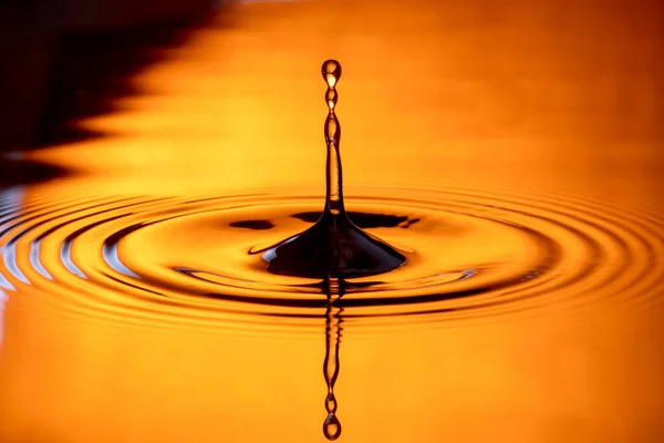 水滴在水滴和倒映水的橙色玻璃杯中飞溅 — 图库照片