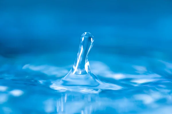 ガラスの青い色の水に水滴が飛び散って水を反射しています — ストック写真