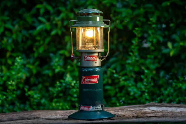 Bangkok, Tayland - 28 Haziran 2021: Eski ahşap masadaki Coleman gaz lambası Arka plan yeşil ağaçlar.