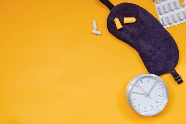 Uyuyan göz maskesi, çalar saat, kulak tıkaçları ve renkli arka planda izole edilmiş uyku hapları..