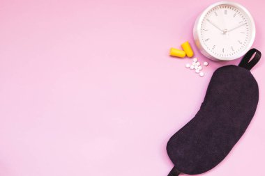 Uyuyan göz maskesi, çalar saat, kulak tıkaçları ve renkli arka planda izole edilmiş uyku hapları veya vitaminler.