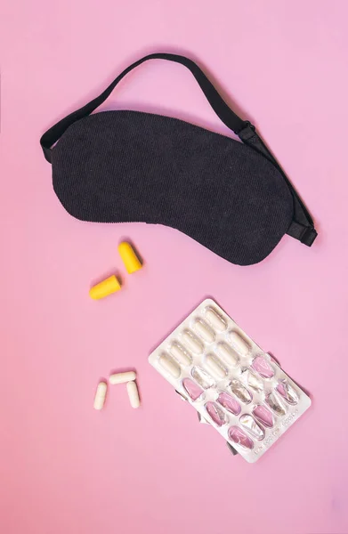 Sleeping eye mask, alarm clock, ear plugs and sleeping pills or vitamins isolated on colourful background.