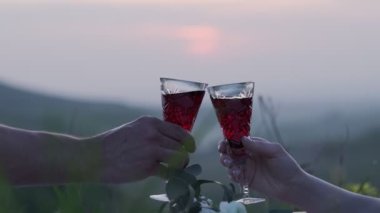 Yeni evliler güneş batarken kırmızı şarapla kristal bardakları tokuştururlar. Ağır çekimde kapat.