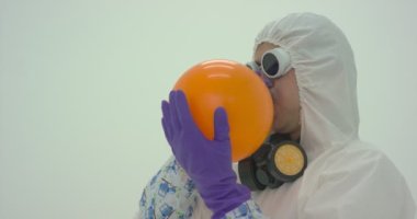 Kimyasal korumalı adam turuncu bir balonu şişiriyor, ağır çekimde.