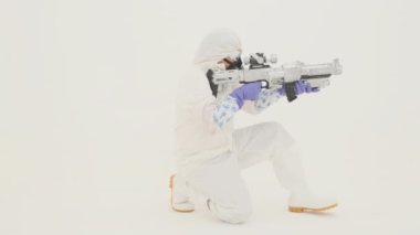 Beyaz kimyasal korumalı süitteki adam sahte saldırı tüfeği ve ağır çekimde hedef alıyor.