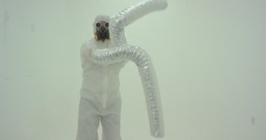 Beyaz duvarın önünde dans eden canavar elleri gibi görünen, uzun kollu, kimyasal korumalı garip bir adam silueti. Yavaş çekim