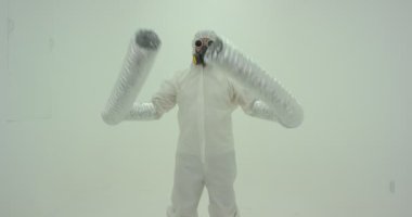 Beyaz duvarın önünde dans eden canavar elleri gibi görünen, uzun kollu, kimyasal korumalı garip bir adam silueti. Yavaş çekim