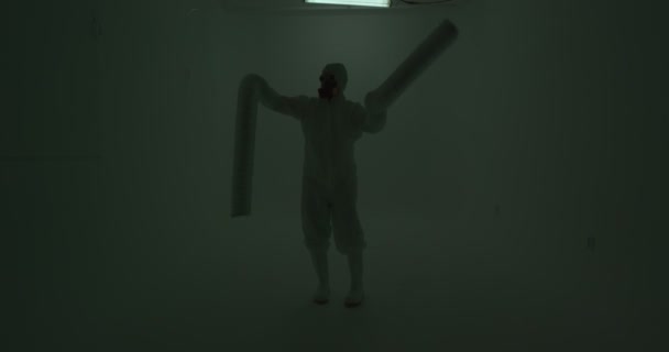 白い壁の前で踊るモンスターの手のように見える非常に長い袖を持つ化学保護スイートの男の奇妙なシルエット スローモーション — ストック動画