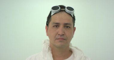 Beyazlı koruyucu gözlüklü bir adam burnundan saçlarını çekip elindeki aynaya bakıyor ve bu onu incitiyor. Kamerayı kapat, yavaş çekim..