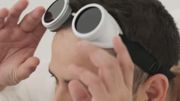 Mężczyzna Bieli Okularami Ochronnymi Głowie Wyciąga Włosy Nosa Patrzy Lustro — Wideo stockowe