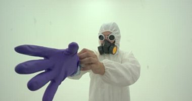 Beyaz kimya koruma giysisi ve gaz maskeli adama yakın çekim menekşe renkli kauçuk koruyucu eldivenlerden birini giyer.