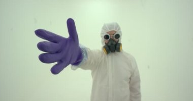 Beyaz kimya koruma giysisi ve gaz maskeli adama yakın çekim menekşe renkli kauçuk koruyucu eldivenlerden birini giyer.