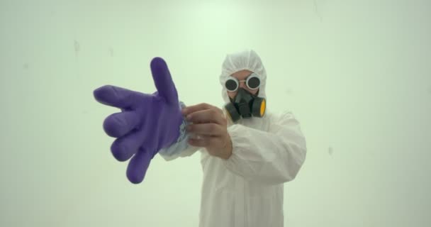 身着白色化学防护服 戴防毒面具的男子特写 戴上紫色橡胶防护手套 动作缓慢 — 图库视频影像