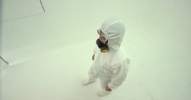 Beyaz kimyasal koruma kıyafeti giyen ve gaz maskesi takmış bir adam kameranın içine giriyor ve yukarıdan çekim yapıyor. Sonra başını sallıyor, baş parmağını kaldırıyor, gaz maskesi takıyor ve kareden çıkıyor..