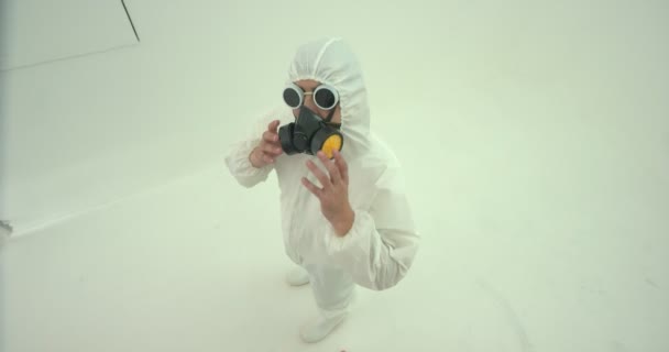 身穿白色化学防护服和防毒面具的男子把头转向从上方拍摄的摄像机 他放下面具 每次都用不同的面部表情盯着摄像机 — 图库视频影像