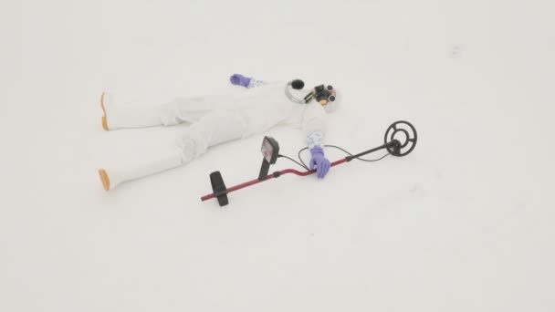 白い化学保護スーツ ガスマスクと紫色のゴム手袋の男が床に横たわっている 彼の近くに金属探知機がある 白地の上から撮影 — ストック動画