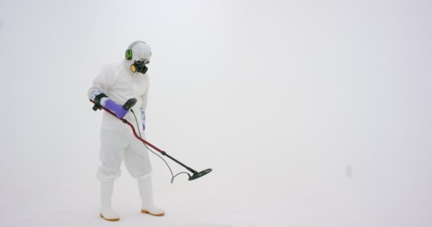 白い化学保護スーツ ガスマスクと紫色のゴム手袋の男は金属探知機を保持し 周りの何かを検索します 白地に撮られた — ストック動画