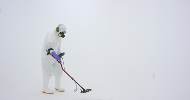 白い化学保護スーツ ガスマスクと紫色のゴム手袋の男は金属探知機を保持し 周りの何かを検索します 白地に撮られた — ストック動画