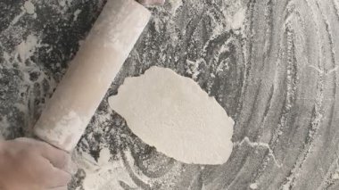 Erkek eller, un serpiştirilmiş ahşap bir tahta üzerinde merdane kullanarak hamur pişirir. Yukarıdan dikey çekim