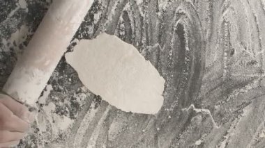 Erkek eller, un serpiştirilmiş ahşap bir tahta üzerinde merdane kullanarak hamur pişirir. Yukarıdan dikey çekim