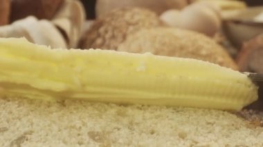 Taze ekmek parçasına tereyağı sürmeye yakın çekim. Arka planda bir sürü ekmek var.