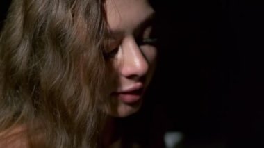 Uzun açık kahverengi saçlı, gri gözlü, beyaz bardaktan zevk alarak kahve içen bir kızın yakın çekimi. Siyah bir arkaplanda tam yüz olarak çekilen