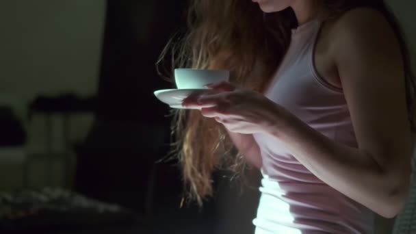 一个有着浅棕色长发 灰色眼睛和长长的睫毛 穿着粉色短裙的女孩 很高兴地喝着一杯白咖啡 侧身中枪 在一间昏暗的房间里拍摄 — 图库视频影像