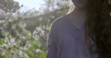 Uzun açık kahverengi saçlı, açık pembe elbiseli gri gözlü kız yaz şapkası ve çiçek açan elma dalı tutuyor. Dalı şapkaya iliştirmeye çalışır ve ondan sonra kokuyu alır. Açık havada, elma bahçelerinde güneşe karşı çekilmiş..