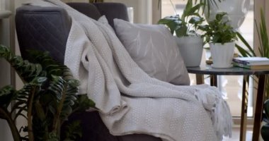 Koyu mor koltuk ve tencere ve kitapların olduğu yuvarlak kahve masası oturma odasının köşesine konur. Çiçek desenli beyaz yastık ve kalın kumaştan yapılmış püsküllü beyaz ekose koltukta.. 