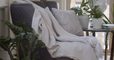 Koyu mor koltuk ve tencere ve kitapların olduğu yuvarlak kahve masası oturma odasının köşesine konur. Çiçek desenli beyaz yastık ve kalın kumaştan yapılmış püsküllü beyaz ekose koltukta.. 