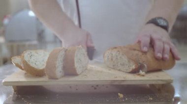 Baker (çerçevedeki erkek eller) taze fırınlanmış Hollanda ekmeğini kuru üzüm ve ekmek bıçağıyla kurutulmuş kayısılarla kesiyor. Kırıntılar kesme tahtasına ve masaya düşmüş..