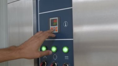 Erkek ellerinin, sanayi ekmek fırını kontrol panelinde düğme ve ekran ve alüminyum görünümlü zaman ve sıcaklık ayarlaması. Kamera elleri takip ediyor.