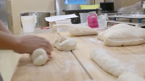 三个面包师 摄影手 用面团在面包店工作 其中一个是电子秤上的面团 之后又有两个人揉搓和塑成了面包片 桌上放着许多面团面包 — 图库视频影像