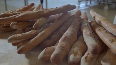 Ahşap masanın üzerinde duran taze ekmeklerin yakın çekimi. Yenileri fırıncı tarafından delikli büyük metal kürek kullanılarak ekleniyor.