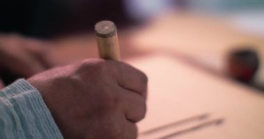 Bir kaligraf stilini mürekkebe batırır ve antik teknolojiyi kullanarak parşömen üzerine bir mektup yazar.