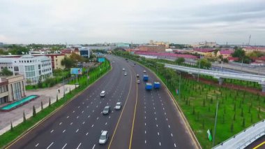 İnsansız hava aracı hareket halindeki arabalarla şehrin yollarında ve otoyollarında uçuyor. Bulutlu bir yaz günü. Hava Görünümü.