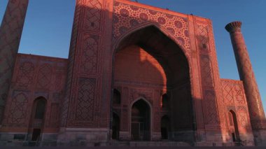 Özbekistan, Semerkant 'taki Bibi-Khanym Camii yakınlarında bir İHA uçuyor. Bina pembe şafak ışığı ile aydınlatılır. Bulutsuz bir sabah. Hava Görünümü.