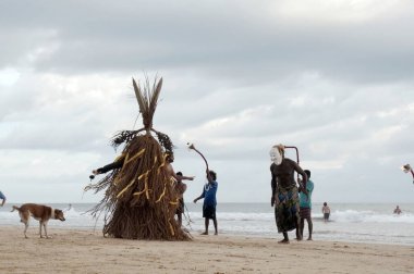 Hikkaduwa, Sri Lanka - 10 Aralık 2015: Beyaz maskeli bir adam okyanus kıyısındaki kumlu bir plajda iyi hava ve iyi balık avlama töreni sırasında kamış heykeliyle dans ediyor.