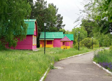 Fenerli asfalt bir yol bir yaz günü ağaçların arasında bir bahçede küçük ahşap turist evlerinin yanından geçer..