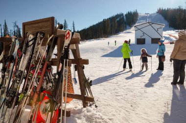 Salanga, Kemerovo bölgesi, RF - 13 Şubat 2017: Kayak ve snowboardlu bir raf güneşli bir kış gününde bir asansör ve kayakçıların bulunduğu bir kayak merkezinin zemininde duruyor.