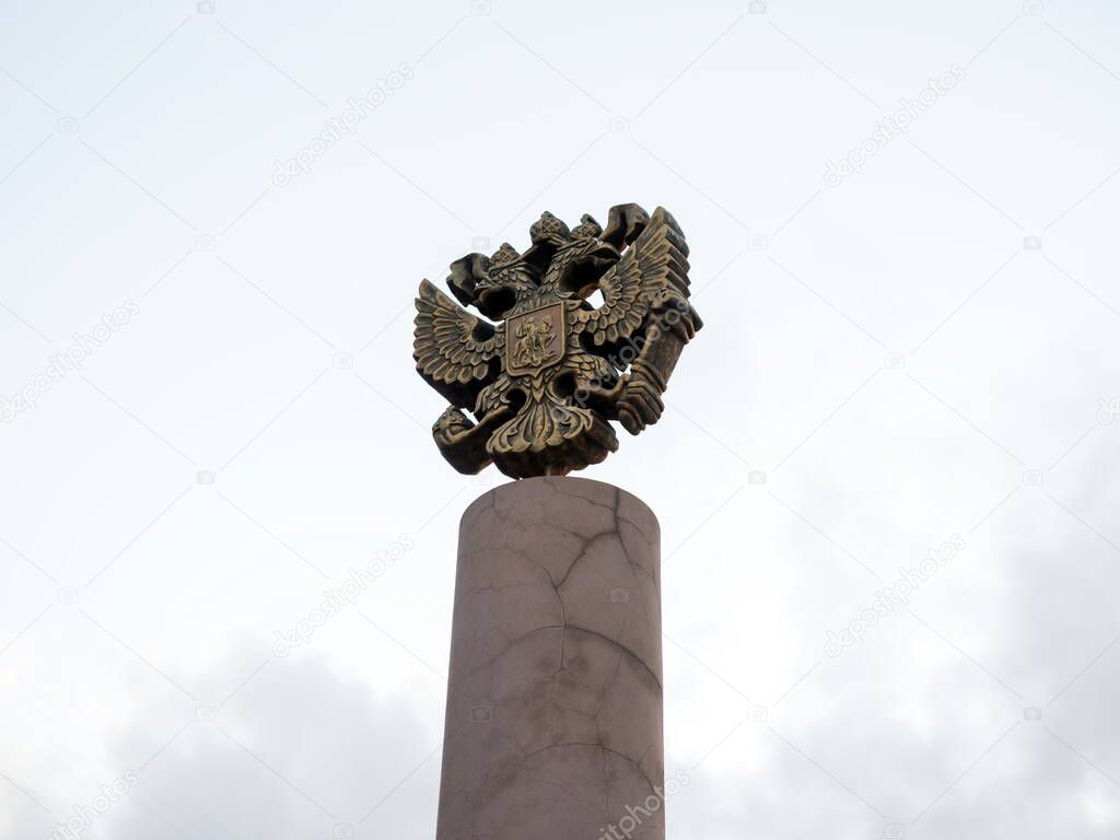The coat of arms of Russia is the official state symbol of the Russian Federation (1993) cast in bronze on the top of the pillar against the sky.