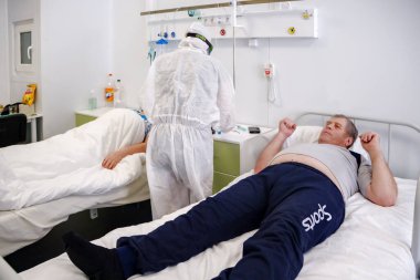 Boguchany, Krasnoyarsk Bölgesi, Rusya - 18 Şubat 2021: COVID-19 'a karşı koruyucu giysi giyen bir doktor, hastanenin bulaşıcı hastalıklar bölümünün hastane koğuşunda yatalak hastaların yanında bulunuyor.