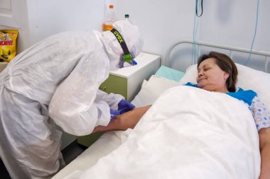 Boguchany, Krasnoyarsk Bölgesi, Rusya - 18 Şubat 2021: COVID-19 'dan koruyucu kıyafetli bir doktor, bir hastanenin bulaşıcı hastalıklar bölümünün hastane koğuşunda yatan bir hastadan test için kan alıyor.