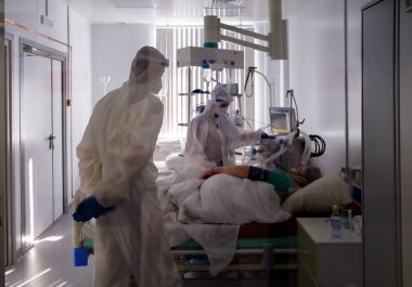 Boguchany, Krasnoyarsk Bölgesi, Rusya - 18 Şubat 2021: COVID-19 'a karşı koruyucu giysiler giyen doktorlar, hastanenin bulaşıcı hastalıklar bölümünün yoğun bakım ünitesinde, solunum cihazında hastanın yanındadır..