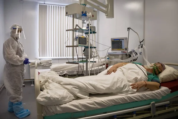 Boguchany, Krasnoyarsk Bölgesi, Rusya - 18 Şubat 2021: COVID-19 'a karşı koruyucu giysi içindeki bir doktor, hastanenin bulaşıcı hastalıklar bölümünün yoğun bakım ünitesinde, solunum cihazında hastanın yanında bulunuyor..