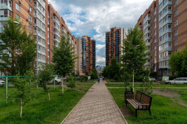 Krasnoyarsk, Krasnoyarsk Bölgesi, RF - 1 Temmuz 2021: Bulutlu bir yaz gününde kadınlar tuğlalı çok katlı apartman binalarının önünden geçerek kaldırımda yürüyorlar.