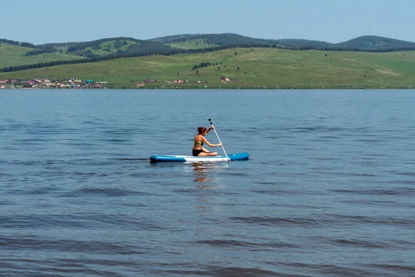 2021年7月4日Rfクラスノヤルスク州シャリポフスキー地区パルナイア 夏の晴れた日に 山間部の海岸を背景に 湖の上のパドルボード Supボード で泳ぐ若い女性 — ストック写真