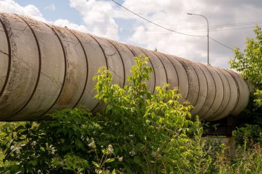 Güneşli bir yaz gününde çimenler arasında güçlendirilmiş beton destek üzerine şehrin ana ısıtma ağının yüzey hattının bir parçası..