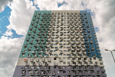 Bulutlu bir gökyüzüne karşı 4 renge boyanmış, balkonları ve pencereleri olan çok katlı yeni bir apartmanın cephesi..