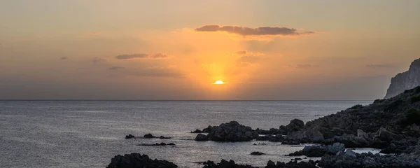 Panorama des Sonnenaufgangs über dem Meer. Die Sonnenstrahlen spiegeln sich in den Wolken wider. Im Vordergrund ein felsiges Ufer — Stockfoto